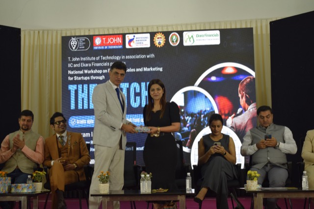 A guest receives a memento in front of THE PITCH banner