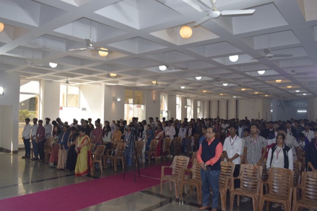 Students and faculty stand in the auditorium as the programme begins