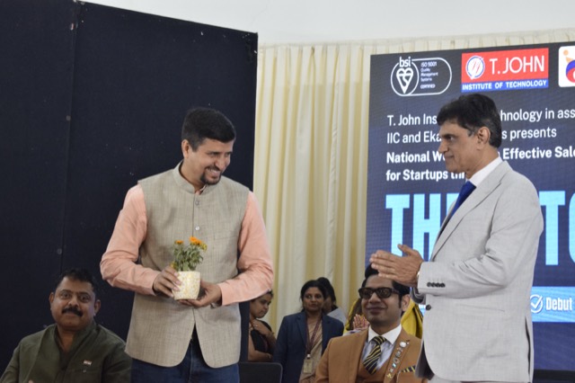 A guest speaker is felicitated with a plant sapling on stage